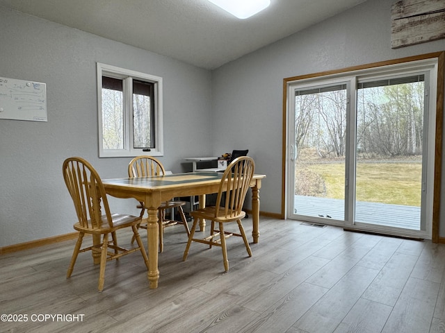 dining room with a textured wall, vaulted ceiling, and light wood-style flooring