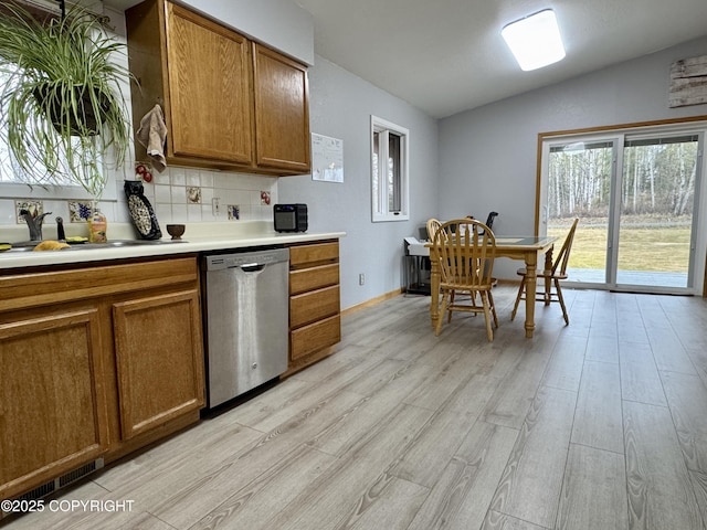 kitchen featuring a sink, brown cabinetry, light wood-style flooring, lofted ceiling, and stainless steel dishwasher
