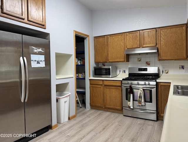 kitchen with appliances with stainless steel finishes, brown cabinets, under cabinet range hood, and light wood finished floors
