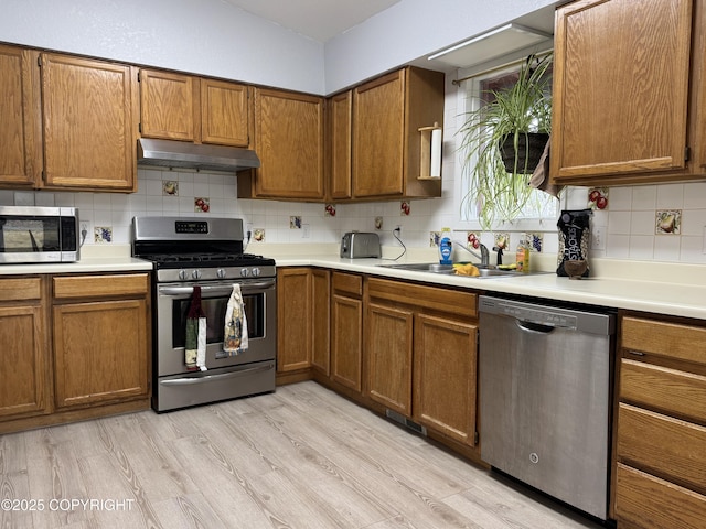 kitchen featuring under cabinet range hood, appliances with stainless steel finishes, brown cabinetry, and a sink