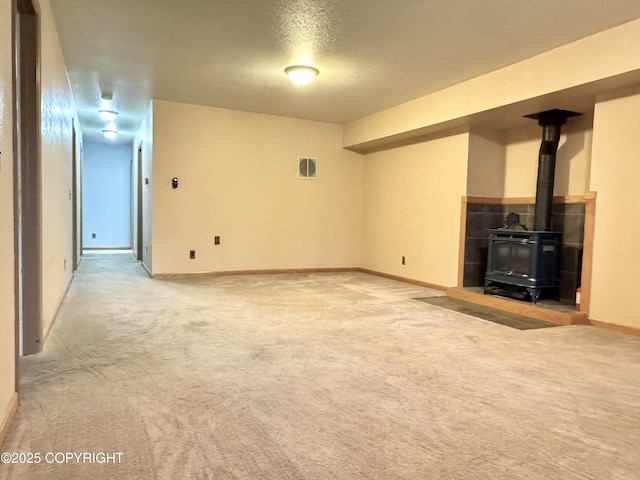 unfurnished living room with visible vents, a wood stove, baseboards, and light colored carpet