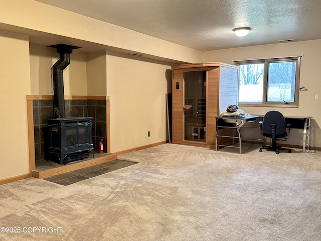 office space with visible vents, a wood stove, baseboards, a textured ceiling, and carpet flooring
