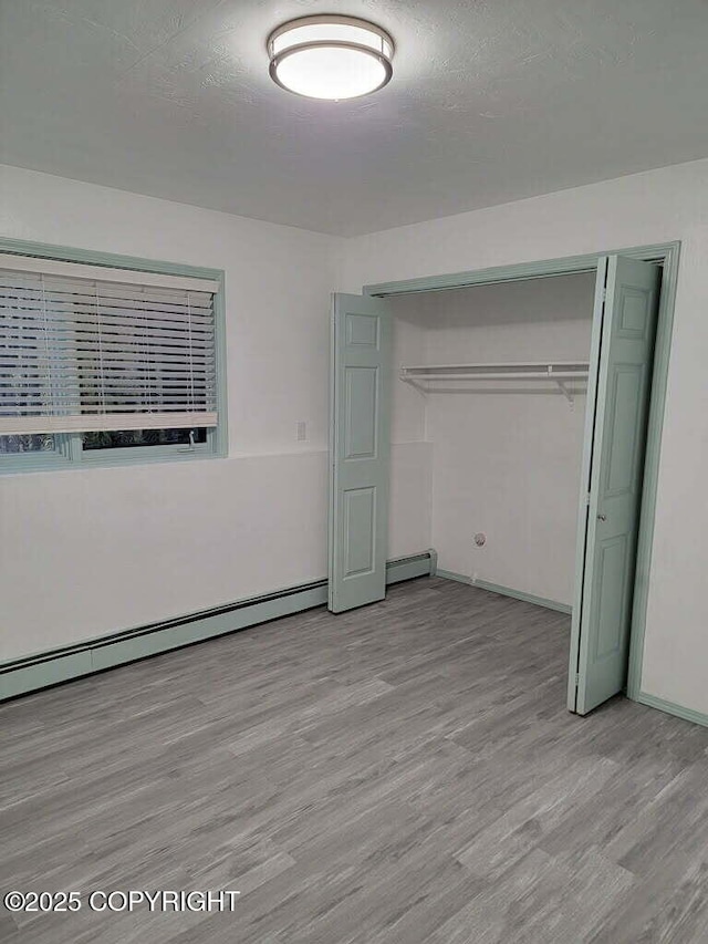 2601 E Quiet Cir, Wasilla, AK 99654 - unfurnished bedroom featuring light wood-type flooring, a baseboard radiator, baseboards, and a closet