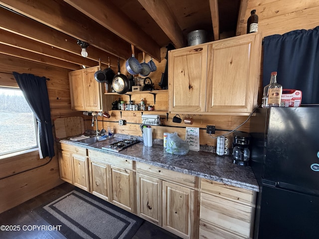 kitchen featuring a sink, light brown cabinets, wooden walls, freestanding refrigerator, and stainless steel gas stovetop