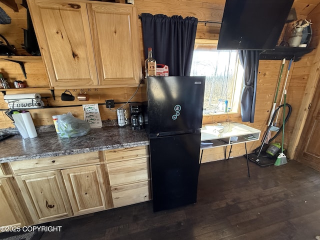 kitchen featuring freestanding refrigerator, light brown cabinets, dark wood-type flooring, wooden walls, and dark stone counters