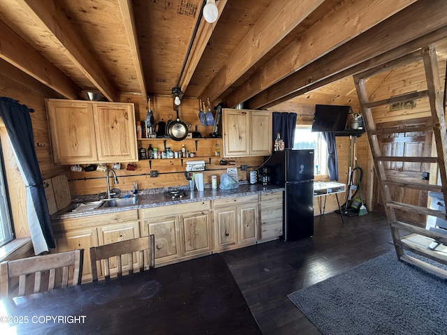 kitchen with a sink, freestanding refrigerator, light brown cabinets, wooden walls, and dark wood finished floors