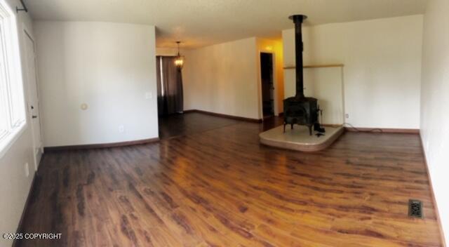 unfurnished living room with a wood stove, visible vents, wood finished floors, and baseboards