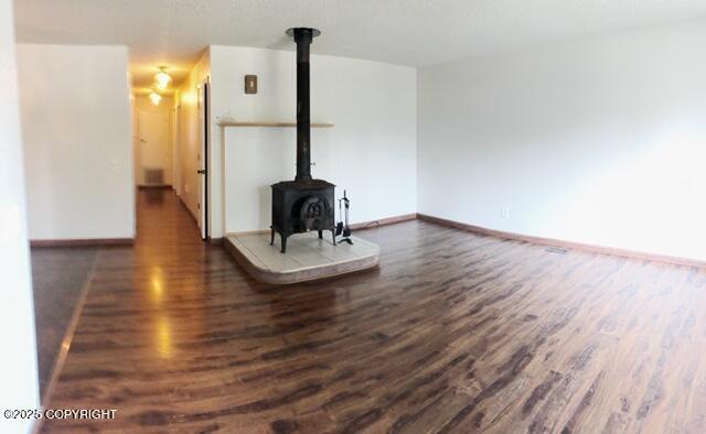 unfurnished living room with baseboards, a wood stove, and dark wood finished floors