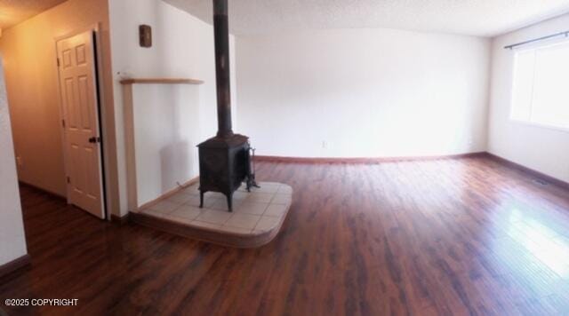 unfurnished living room featuring baseboards, a wood stove, and wood finished floors