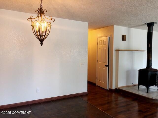 dining room with a wood stove, a notable chandelier, baseboards, a textured ceiling, and wood finished floors