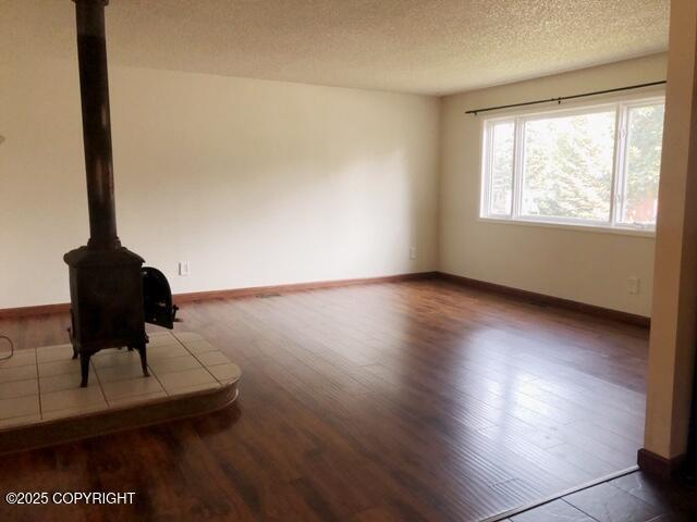 unfurnished living room featuring baseboards, a wood stove, wood finished floors, and a textured ceiling