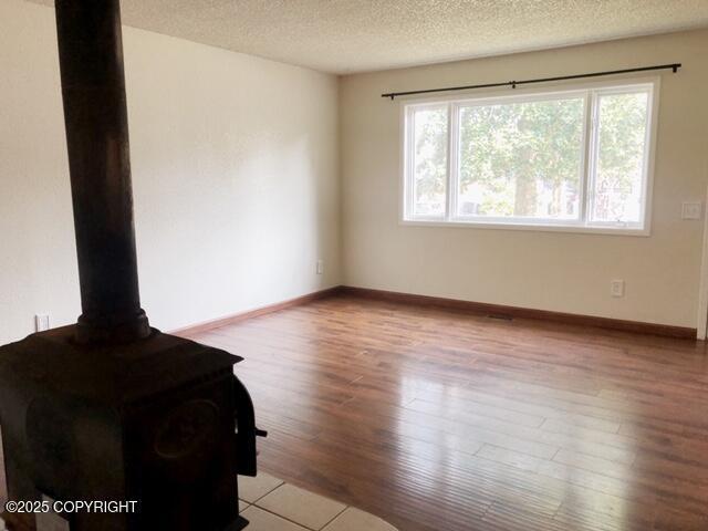 unfurnished living room featuring baseboards, a wood stove, wood finished floors, and a textured ceiling