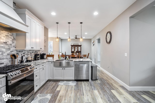 kitchen featuring a sink, light wood finished floors, stainless steel appliances, a peninsula, and custom exhaust hood