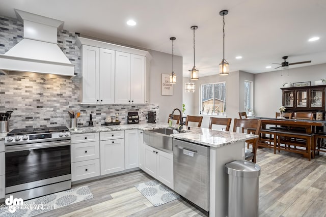 kitchen featuring ceiling fan, appliances with stainless steel finishes, a sink, custom exhaust hood, and a peninsula