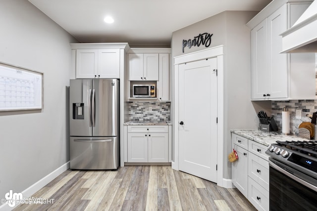 kitchen with white cabinetry, tasteful backsplash, light stone counters, light wood finished floors, and appliances with stainless steel finishes