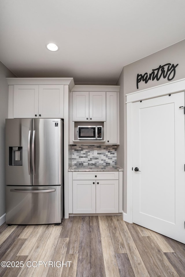 kitchen featuring decorative backsplash, stainless steel refrigerator with ice dispenser, light countertops, recessed lighting, and light wood-style flooring