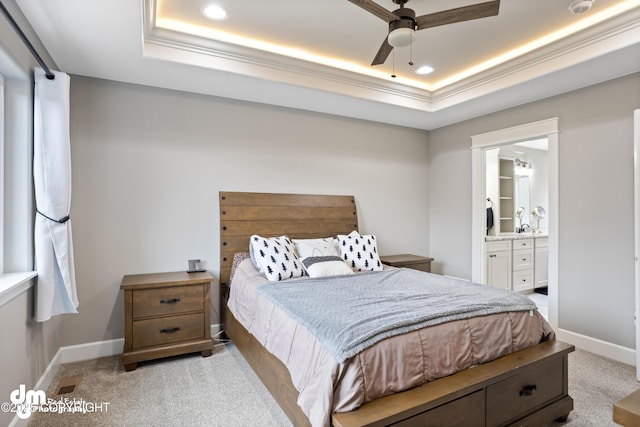 bedroom featuring a raised ceiling, baseboards, ensuite bathroom, and light colored carpet