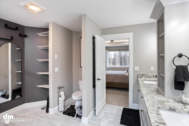 ensuite bathroom with connected bathroom, toilet, baseboards, and double vanity