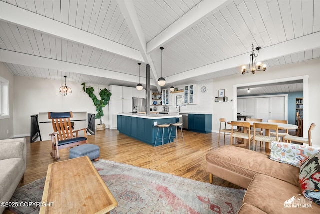 living area with baseboards, lofted ceiling with beams, light wood-style flooring, and a chandelier