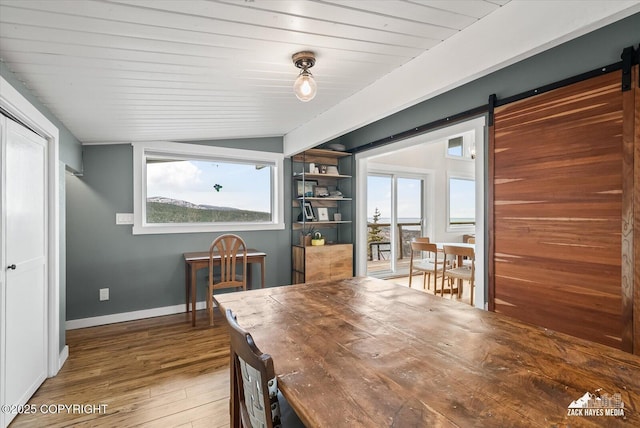 dining space with baseboards, a barn door, vaulted ceiling, and hardwood / wood-style flooring