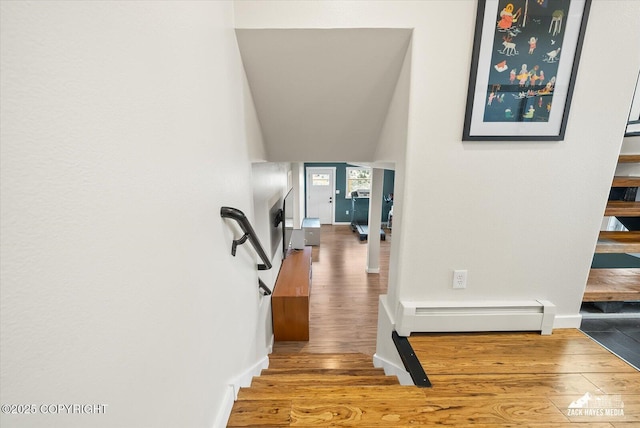 staircase featuring baseboards, wood finished floors, and a baseboard radiator