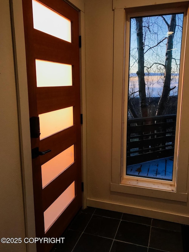 doorway to outside featuring dark tile patterned flooring and baseboards