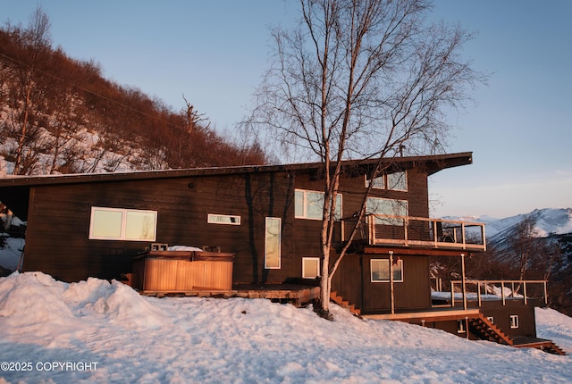 snow covered back of property with a hot tub and a deck