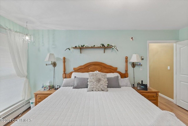 bedroom featuring wood finished floors, baseboards, a baseboard heating unit, and an inviting chandelier