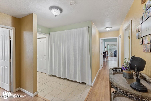 corridor featuring light wood-style floors, baseboards, a textured wall, and a textured ceiling