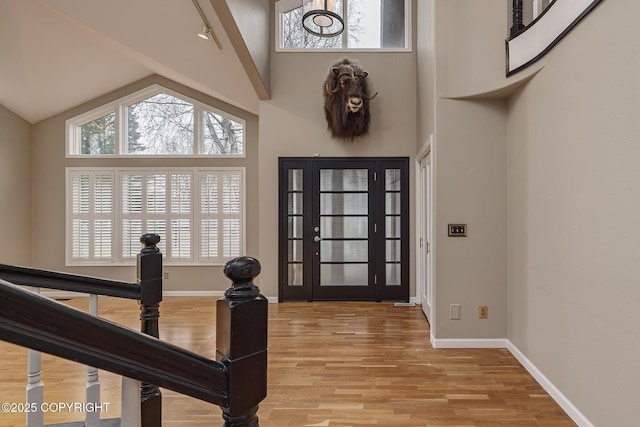 foyer entrance featuring baseboards, high vaulted ceiling, and light wood-type flooring
