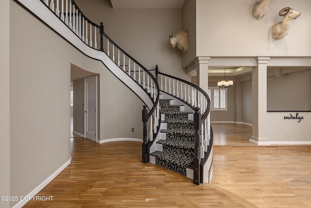 stairway with an inviting chandelier, ornate columns, wood finished floors, and a towering ceiling
