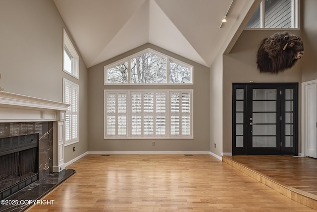 unfurnished living room featuring a premium fireplace, baseboards, vaulted ceiling, and wood finished floors