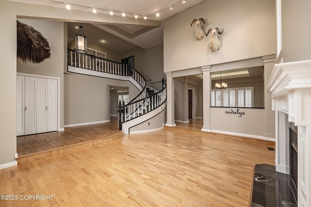 unfurnished living room with a towering ceiling, a chandelier, wood finished floors, and a fireplace