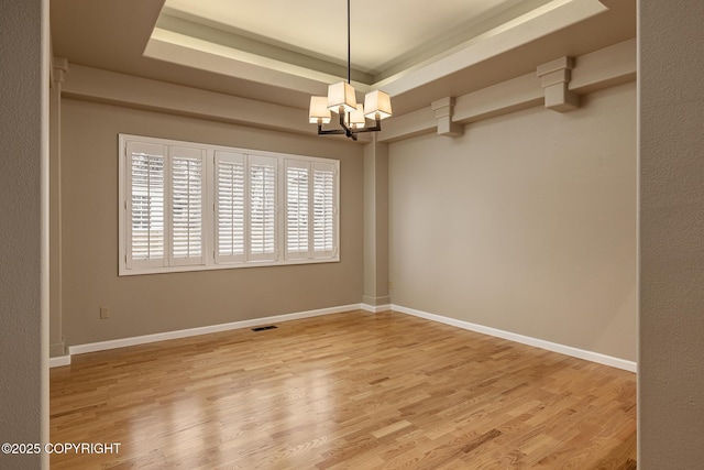 unfurnished room with visible vents, wood finished floors, baseboards, an inviting chandelier, and a tray ceiling