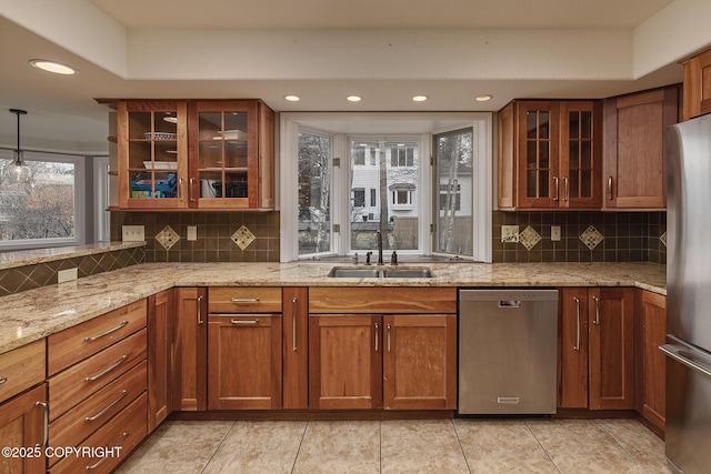 kitchen featuring appliances with stainless steel finishes, light stone counters, a sink, decorative backsplash, and glass insert cabinets