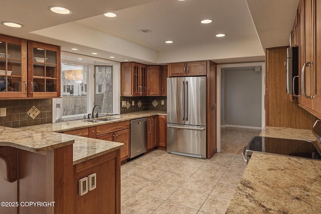 kitchen with decorative backsplash, brown cabinetry, appliances with stainless steel finishes, a sink, and light stone counters