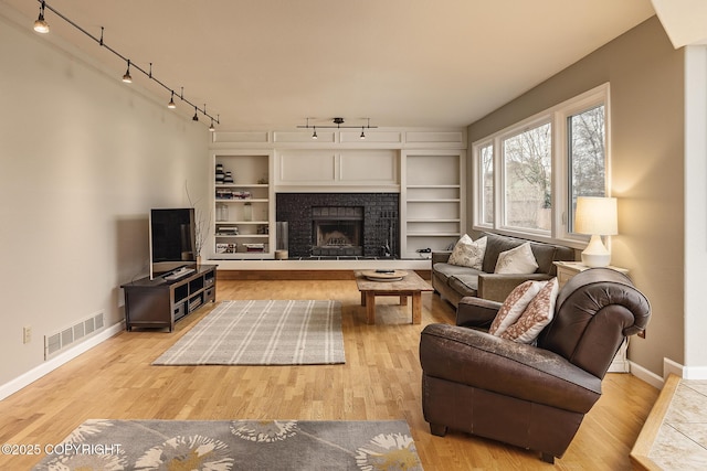 living room featuring track lighting, a fireplace, baseboards, wood finished floors, and visible vents