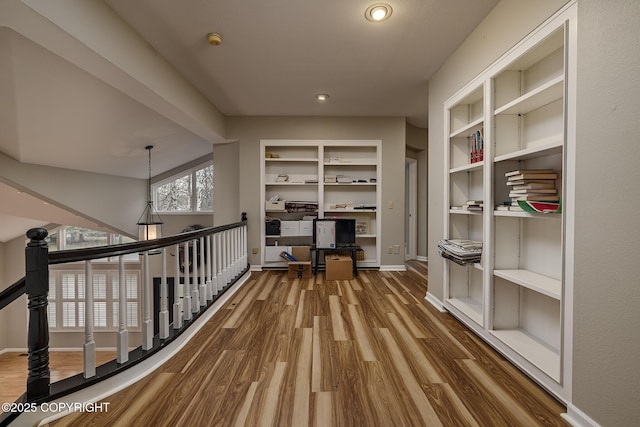 hall with wood finished floors, baseboards, recessed lighting, built in shelves, and an upstairs landing