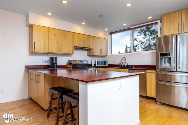 5201 E Northern Lights Blvd # 3N, Anchorage, AK 99508 - kitchen with light wood-style flooring, under cabinet range hood, a sink, a kitchen breakfast bar, and appliances with stainless steel finishes