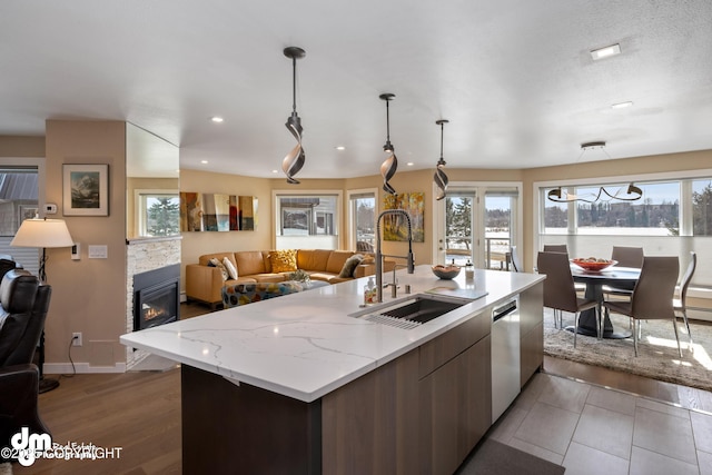 1741 W 15th Ave, Anchorage, AK 99501 - kitchen featuring stainless steel dishwasher, a fireplace, open floor plan, an island with sink, and a sink