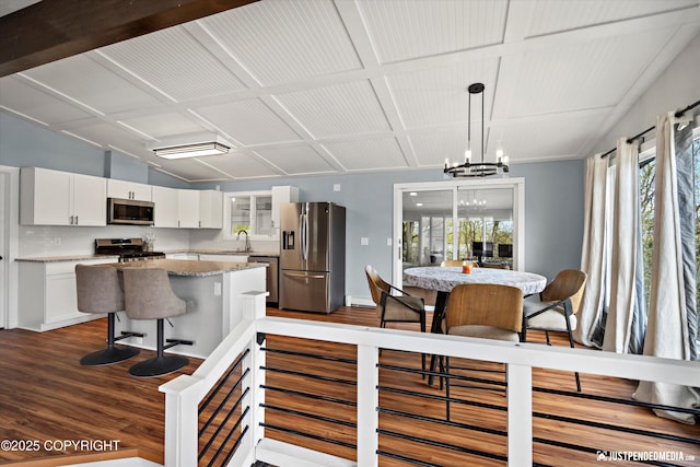 kitchen featuring appliances with stainless steel finishes, dark wood-style flooring, white cabinetry, a chandelier, and a center island