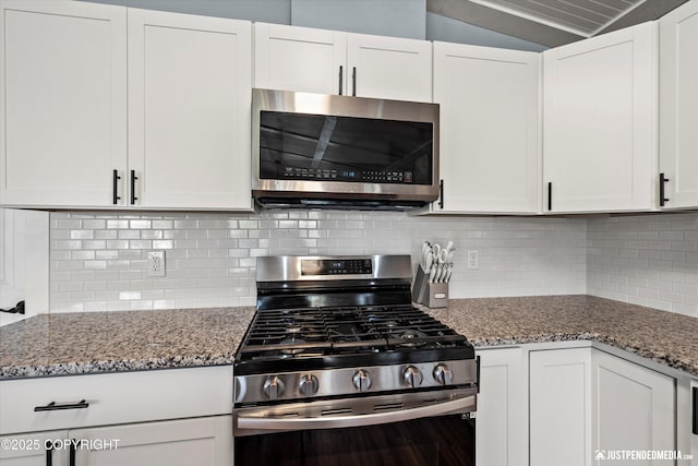 kitchen with appliances with stainless steel finishes, white cabinetry, stone counters, decorative backsplash, and vaulted ceiling