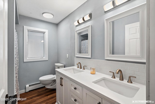 bathroom featuring a baseboard radiator, decorative backsplash, toilet, wood finished floors, and double vanity