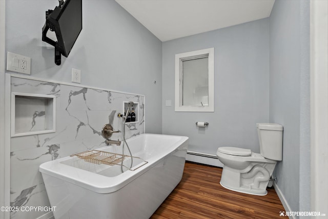 bathroom featuring baseboard heating, a freestanding tub, toilet, wood finished floors, and baseboards