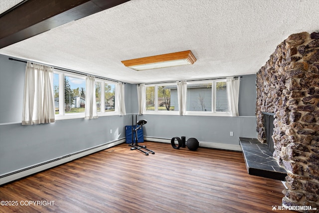 unfurnished room featuring a textured ceiling, a baseboard radiator, wood finished floors, a fireplace, and baseboards