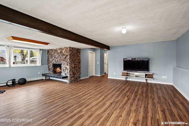 unfurnished living room with a textured ceiling, wood finished floors, a stone fireplace, baseboards, and beamed ceiling