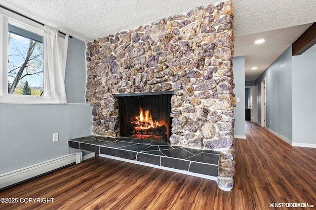 detailed view of a textured ceiling, wood finished floors, a tiled fireplace, a baseboard radiator, and baseboards