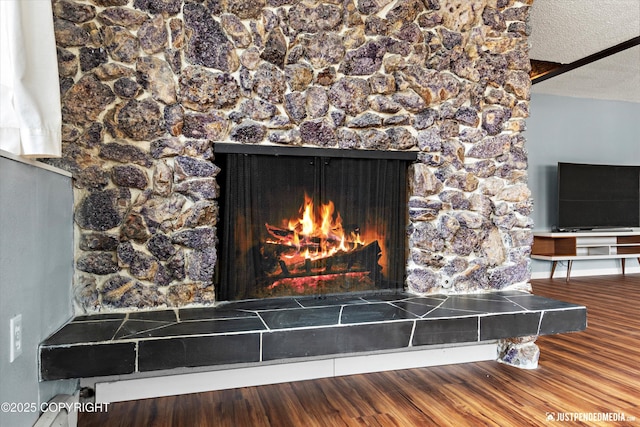 detailed view of a lit fireplace, wood finished floors, and a textured ceiling