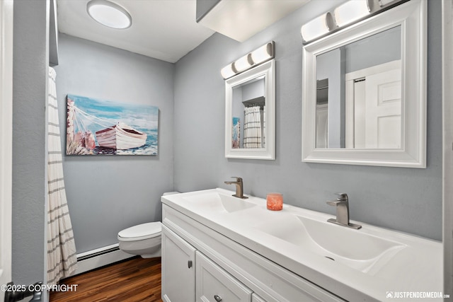 full bathroom featuring toilet, wood finished floors, double vanity, and a baseboard heating unit