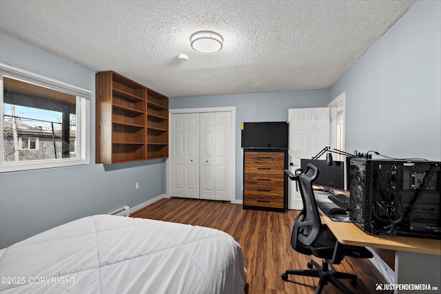 bedroom with a closet, a textured ceiling, dark wood finished floors, baseboard heating, and an office area